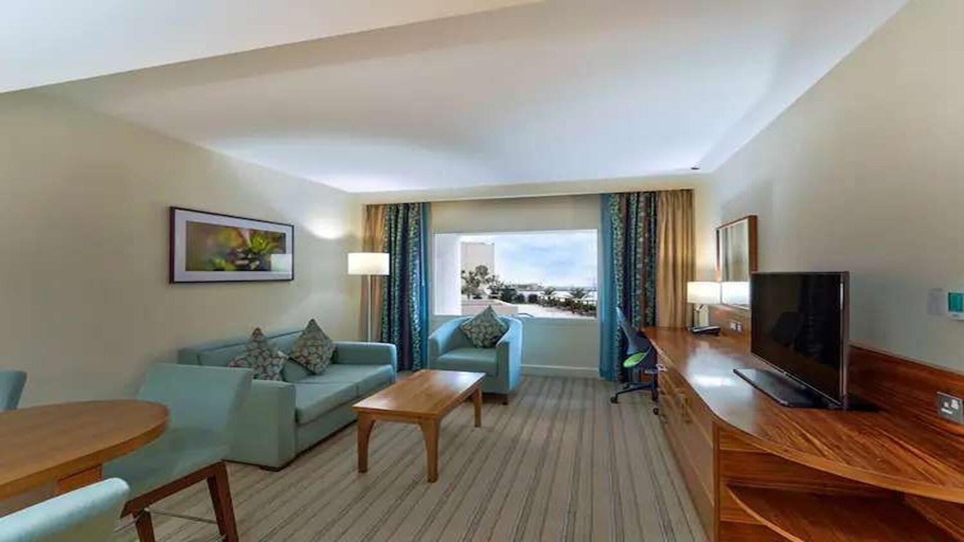 Spacious living area with TV screen, desk and sofa in a king room at the Hilton Ras Al Khaimah Beach Resort.