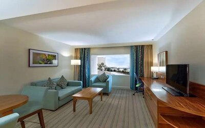 Spacious living area with TV screen, desk and sofa in a king room at the Hilton Ras Al Khaimah Beach Resort.