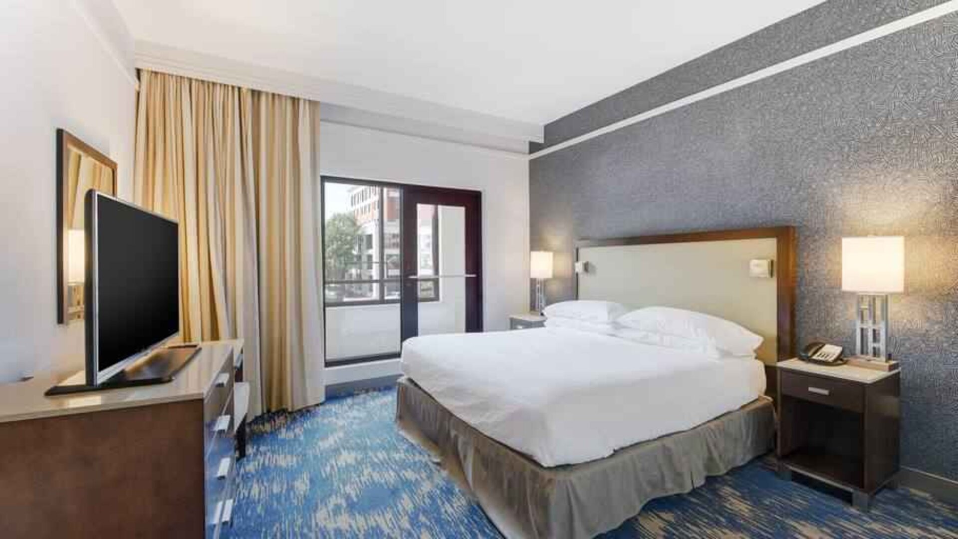 King size bed, large window and TV screen in a king room at the Embassy Suites by Hilton Alexandria-Old Town.