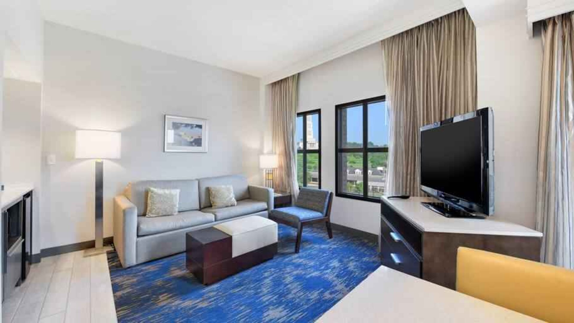 Spacious living room with desk, sofa, TV screen and windows at the Embassy Suites by Hilton Alexandria-Old Town.