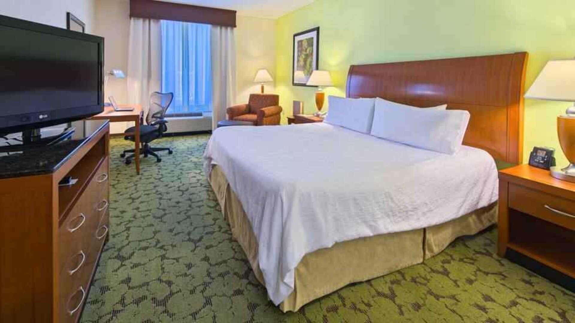 King size bed, TV screen and desk in a hotel room at the Hilton Garden Inn Tallahassee Central.