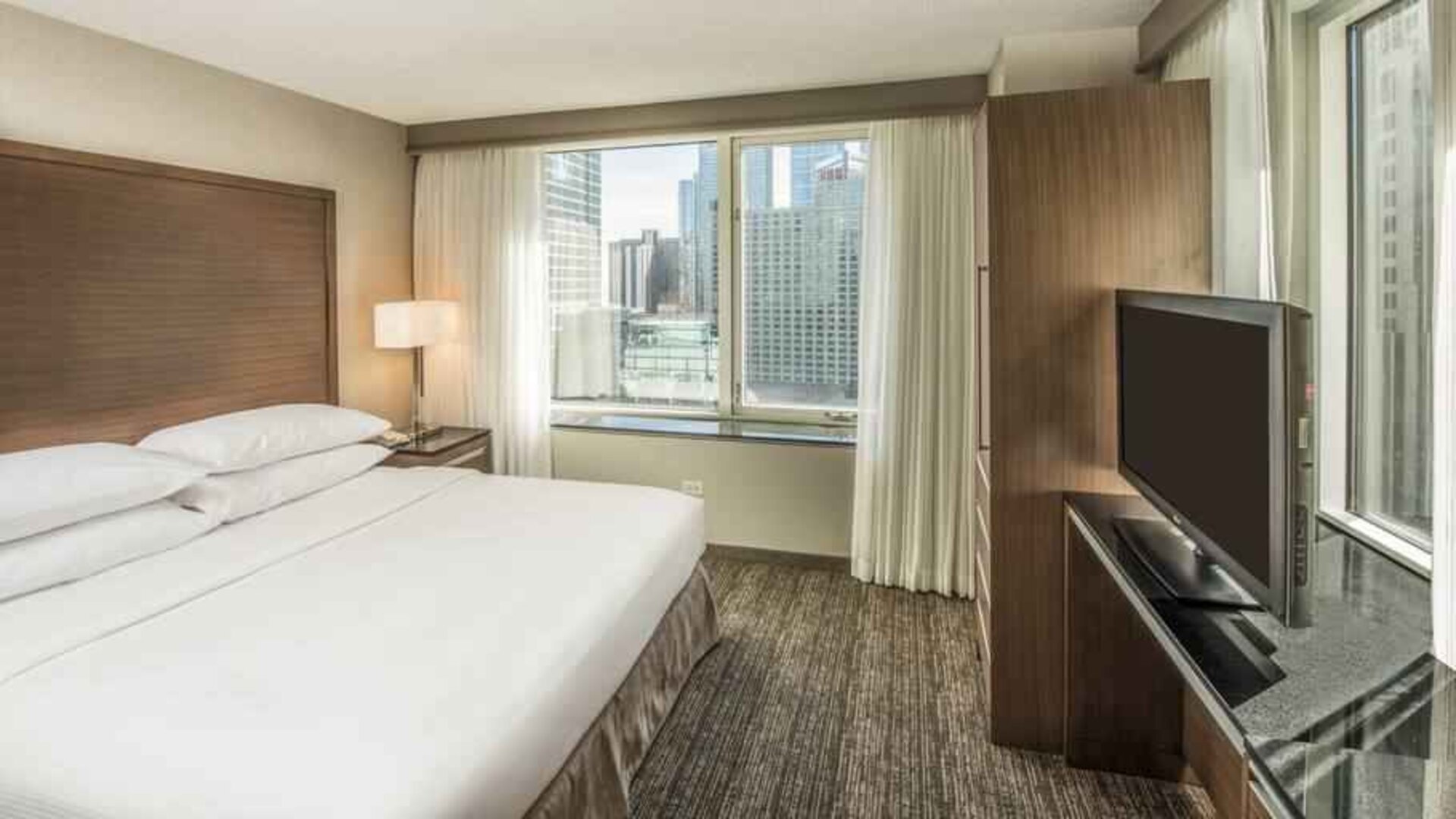 King size bed, TV screen and large window in a bedroom at the Embassy Suites by Hilton Chicago Magnificent Mile.