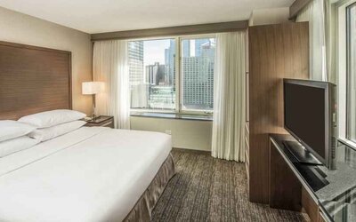 King size bed, TV screen and large window in a bedroom at the Embassy Suites by Hilton Chicago Magnificent Mile.