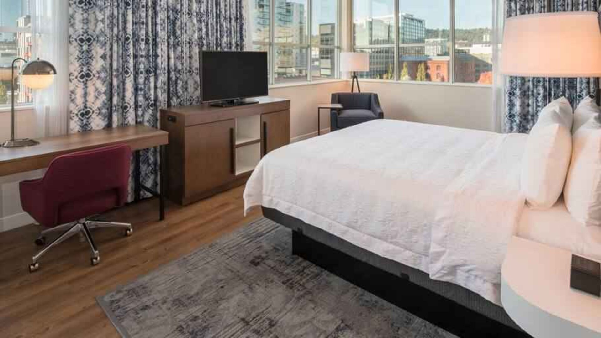 Queen size bed and working station in a hotel room at the Hampton Inn & Suites by Hilton Portland-Pearl District.