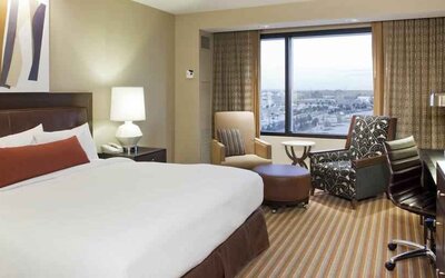 King size bed, TV screen, sofa and desk in a hotel room with window at the Hilton Omaha.