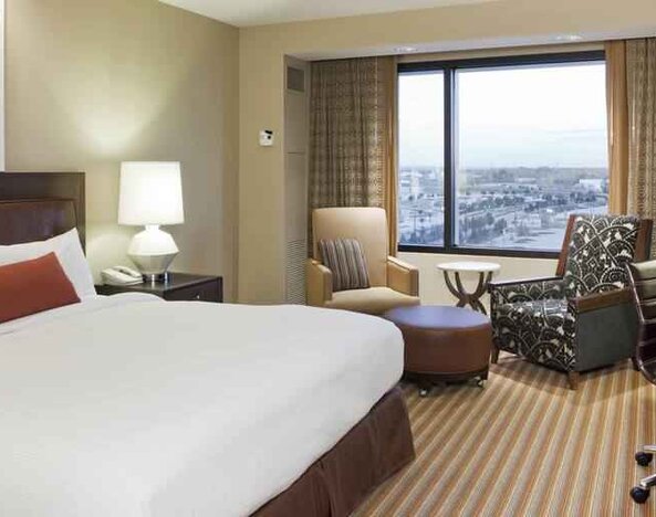King size bed, TV screen, sofa and desk in a hotel room with window at the Hilton Omaha.