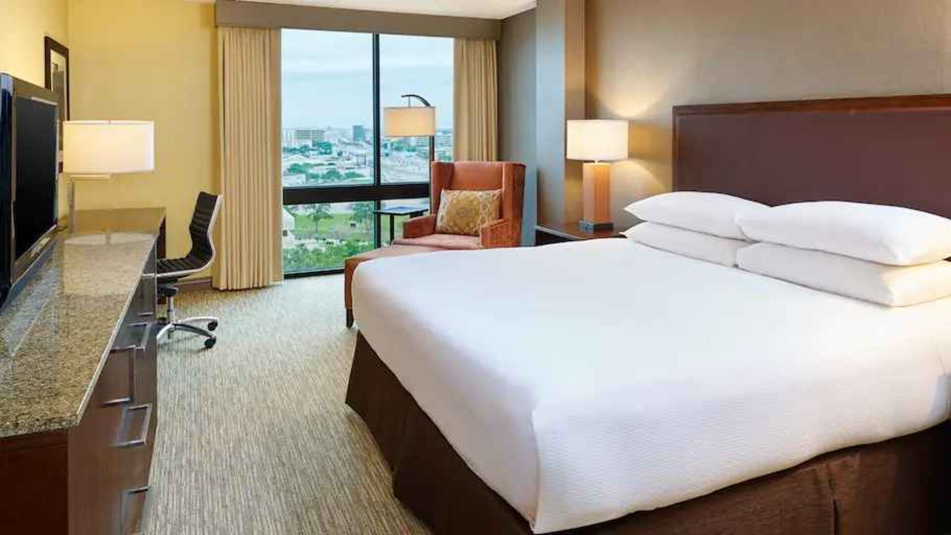 King size bed, desk and TV screen in a king guestroom at the Hilton San Antonio-Airport.
