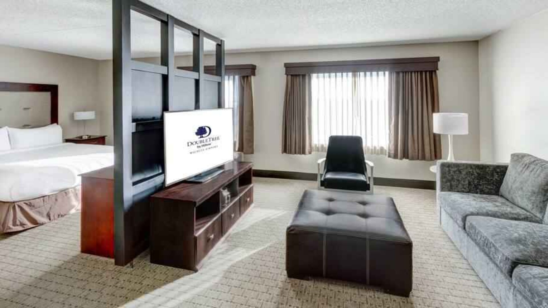 Spacious king suite with TV screen and sofa at the DoubleTree by Hilton Wichita Airport.
