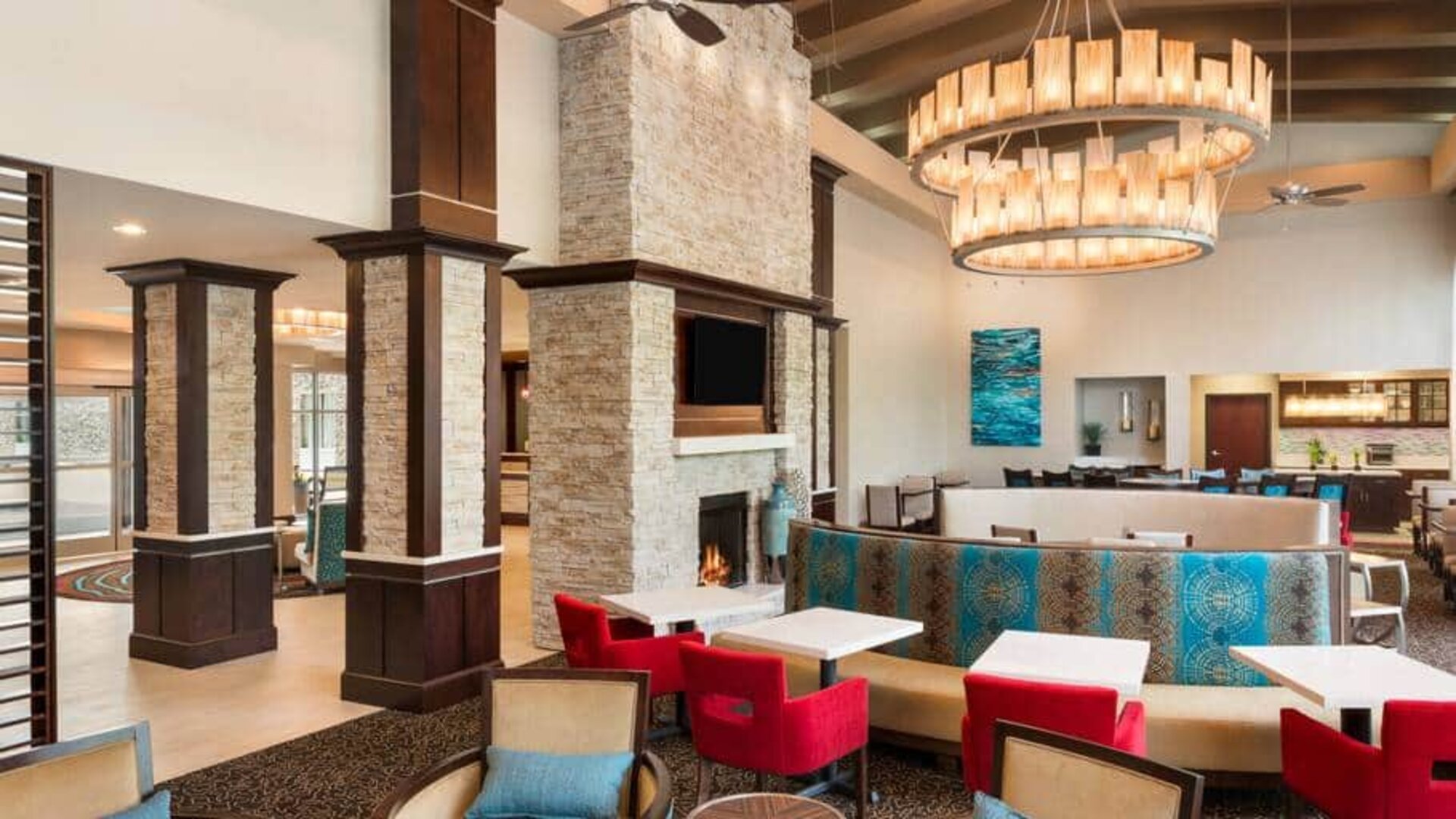 Colorful chairs and booths to eat, socialize or work at. Bright spacious area with large fireplace and chandelier overhead.