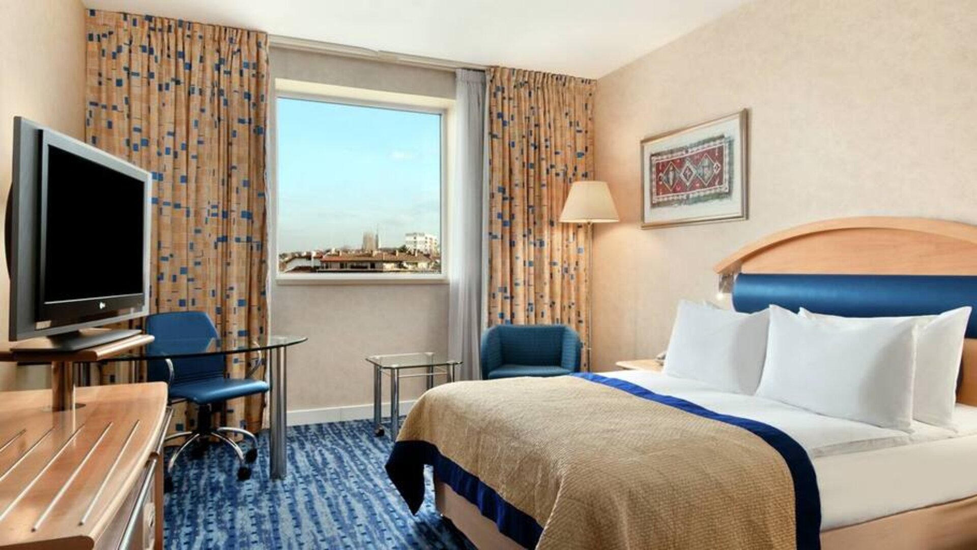 Queen-size bed, desk area, television and window view of city.