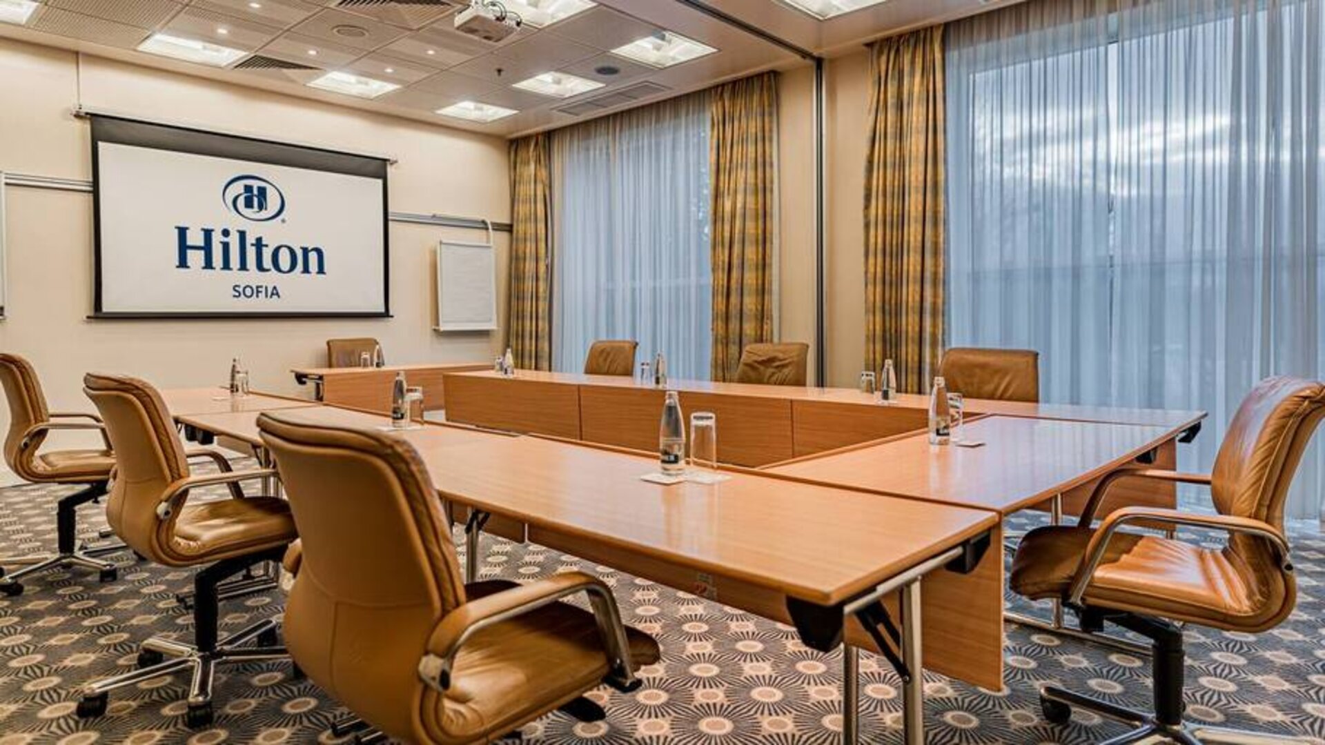 Long u-shaped light brown wooden table with seating for 8-10 guests.
