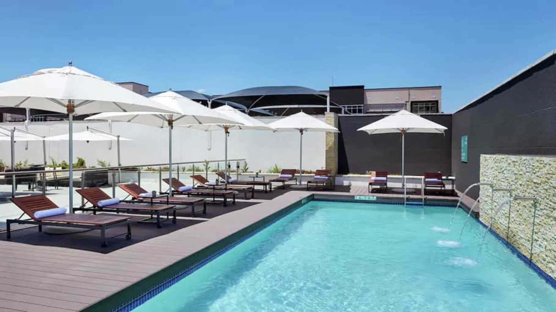 Narrow rectangular pool with fountains coming out of side wall, abundant lounge chairs for sunbathing.