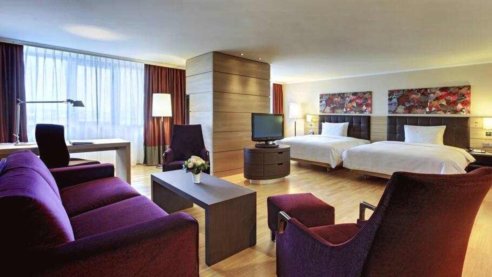 Spacious twin room with beds, desk, TV screen and sofa at the Hilton Mainz.