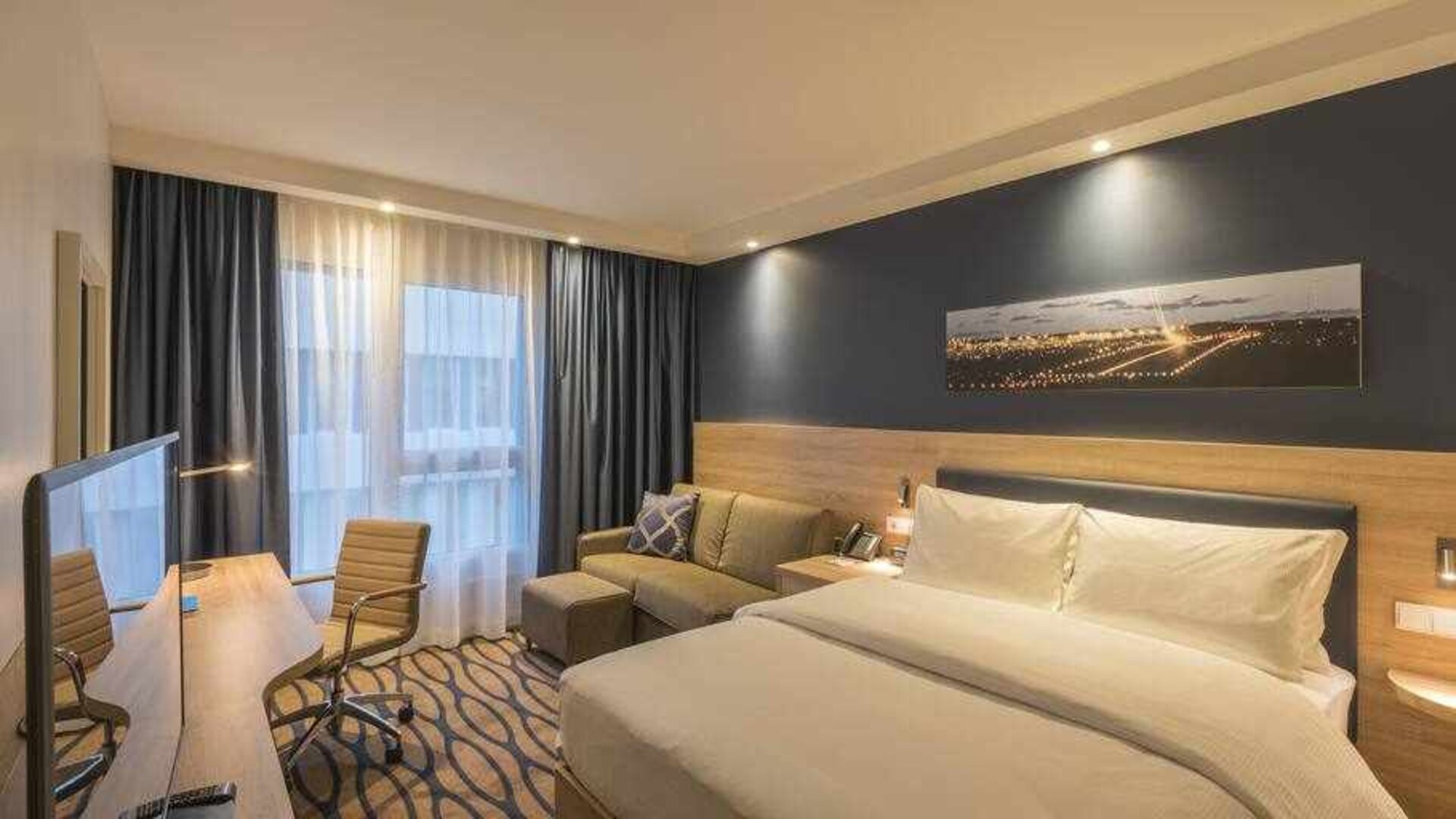 Queen room with sofa and desk at the Hampton by Hilton Frankfurt Airport.