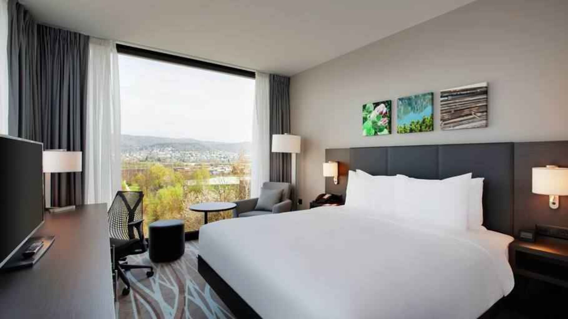 Bright king bedroom with desk along the window at the Hilton Garden Inn Zurich Limmattal.
