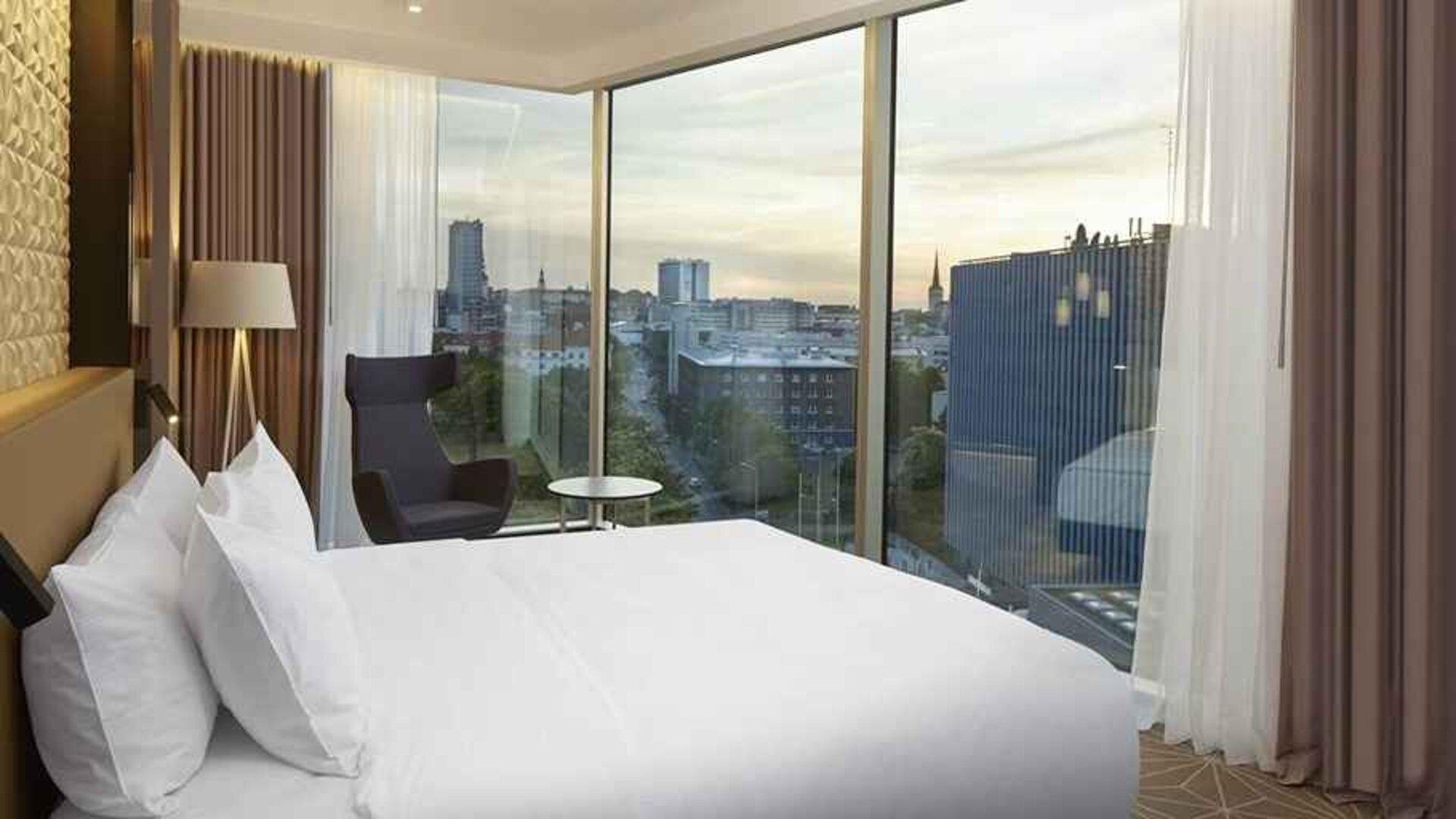 delux king bed with chair and city views at Hilton Tallinn Park.