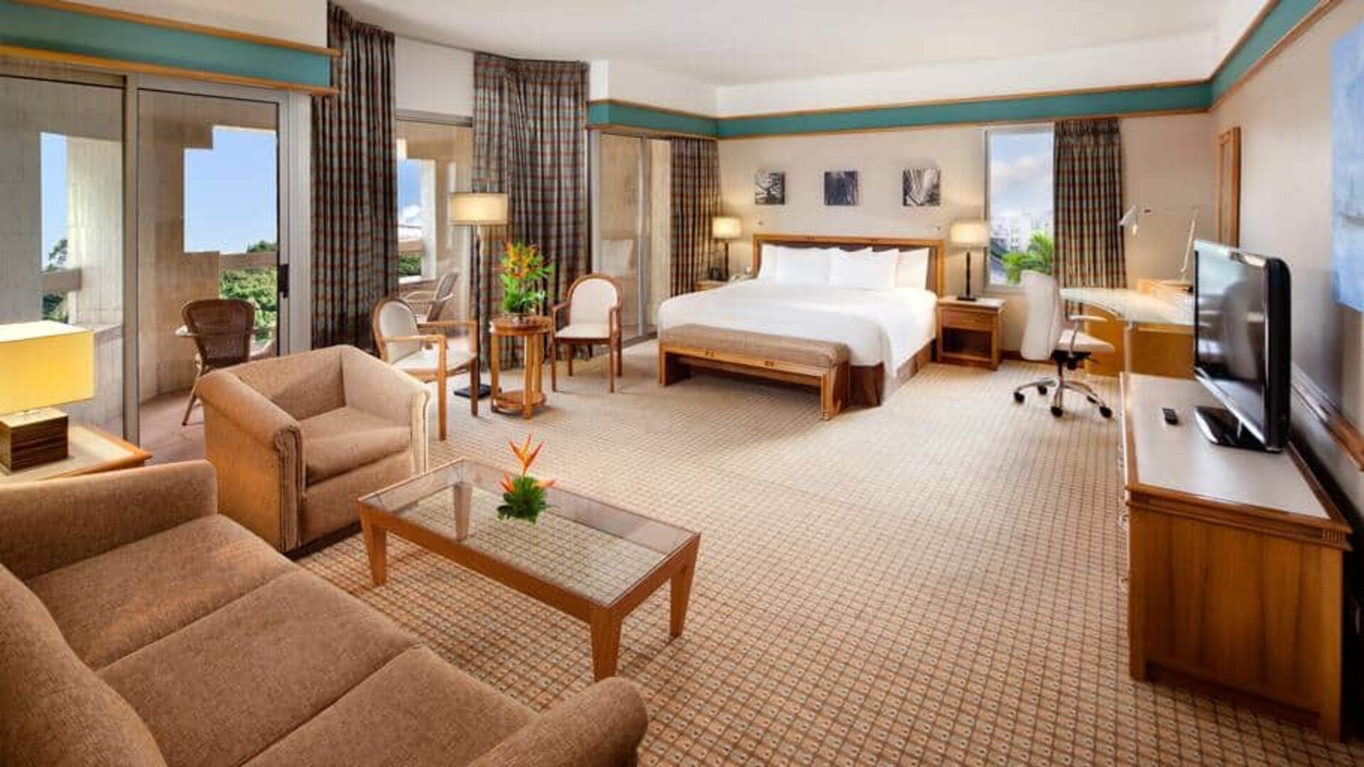 Spacious king suite with king bed, city view, sliding doors, desk, chairs, media console and tv, and sofabed at the Hilton Yaounde.