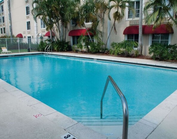 Outdoor pool area surrounded by tropical landscaping, creating a refreshing setting for relaxation and leisure at La Quinta Inn & Suites By Wyndham Sawgrass Mills.