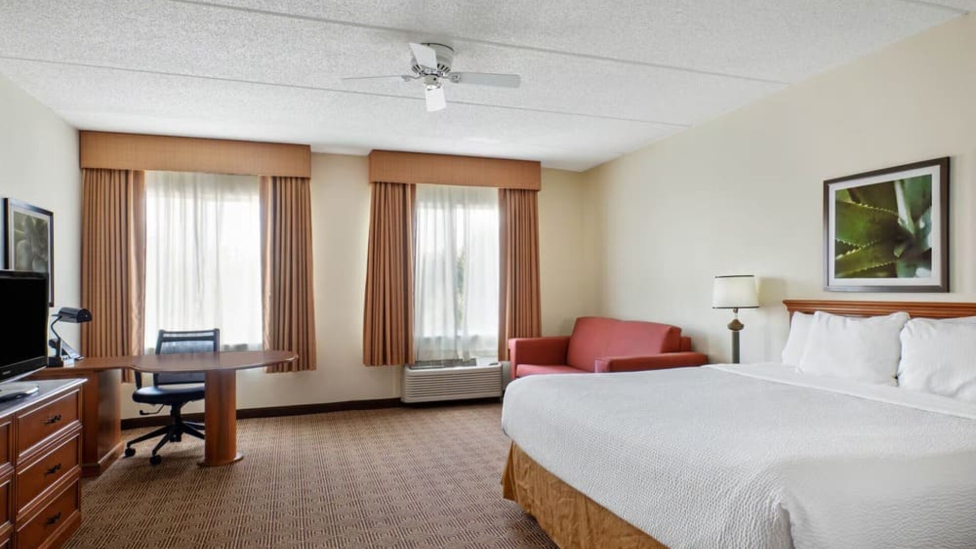 Large guest room featuring a king-size bed, separate seating area, work desk, and ample floor space, providing comfort and convenience for both short and extended stays at La Quinta Inn & Suites By Wyndham Sawgrass Mills.