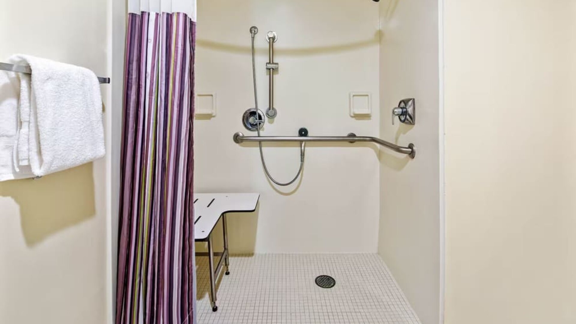 Accessible roll-in shower equipped with grab bars, a handheld showerhead, and a built-in shower seat, designed to provide safety, comfort, and convenience for all guests.