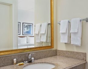 Bathroom vanity area featuring a granite countertop, large framed mirror, fresh towels, and complimentary toiletries, providing guests with a convenient and comfortable space to prepare for the day.