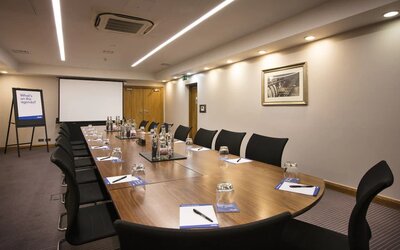 A wider shot of the meeting room with over half a dozen chairs, multiple tables, and a screen.