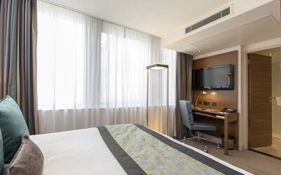 Brightly lit room with king bed and workspace with wall-mounted flat screen TV above.