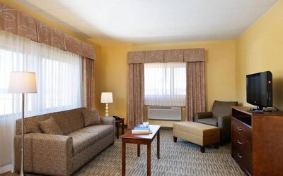 Guest room lounge in Holiday Inn Express Philadelphia Airport, with sofa, chair, TV, and foot stool.