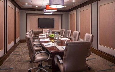 Hotel meeting room, featuring long wooden table and surrounding leather chairs.