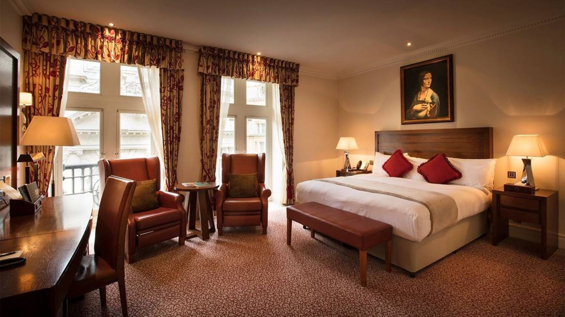 Deluxe king room at The Royal Horseguards Hotel, featuring numerous leather chairs, large windows, and a desk.