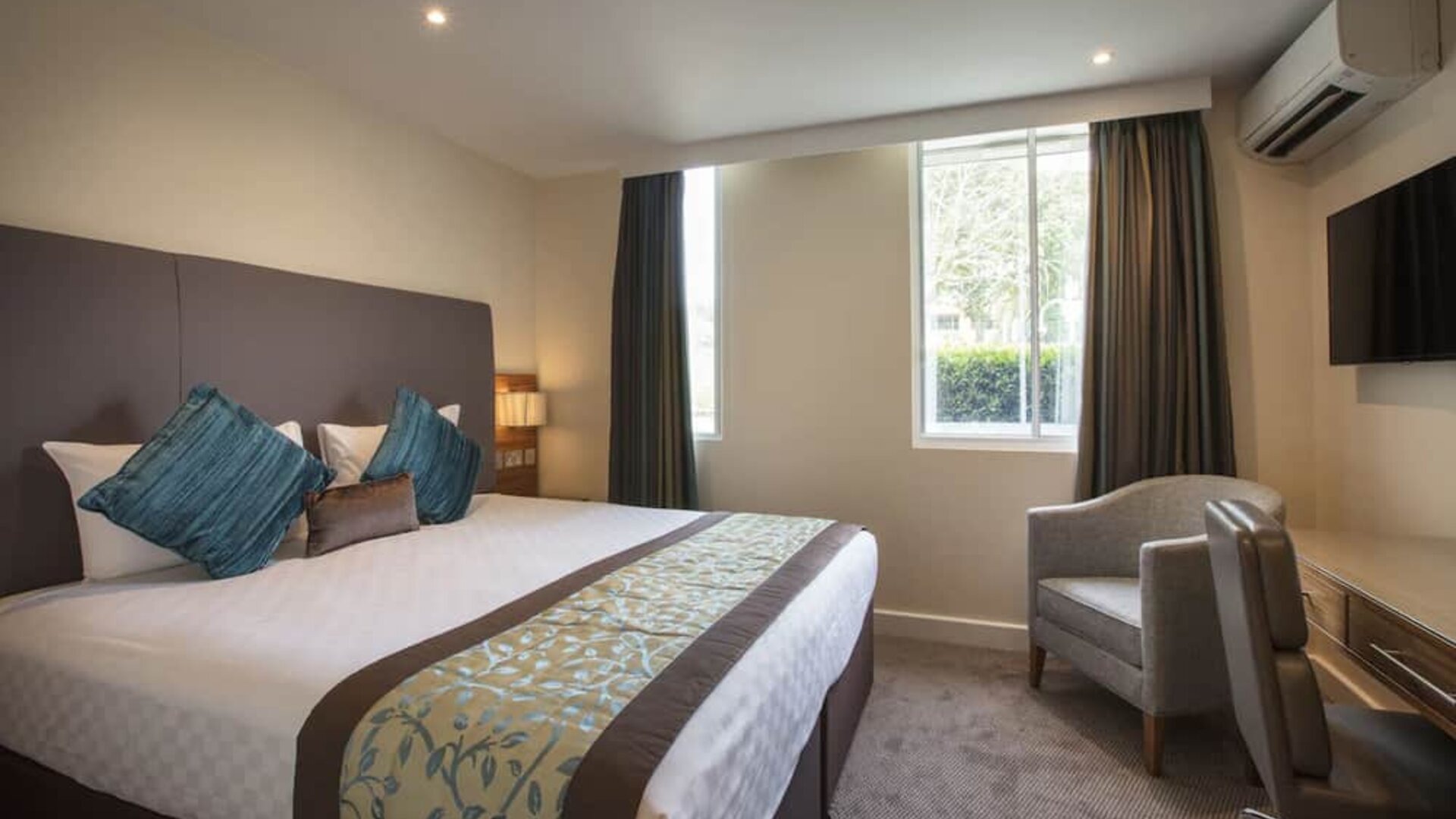 King-size bed with wall-mounted television in upper wall corner and a desk to work from.