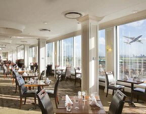 Sunlight room with floor to ceiling windows spanning the entire length of the wall to see planes takeoff and land at London Heathrow Airport.