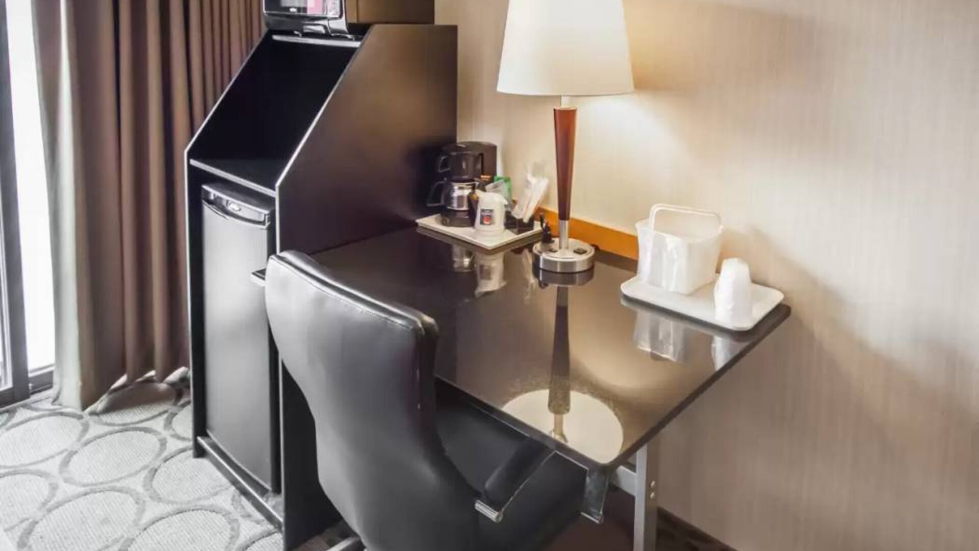 Closer shot of an in-room workspace, including chair, desk, lamp, and nearby window.