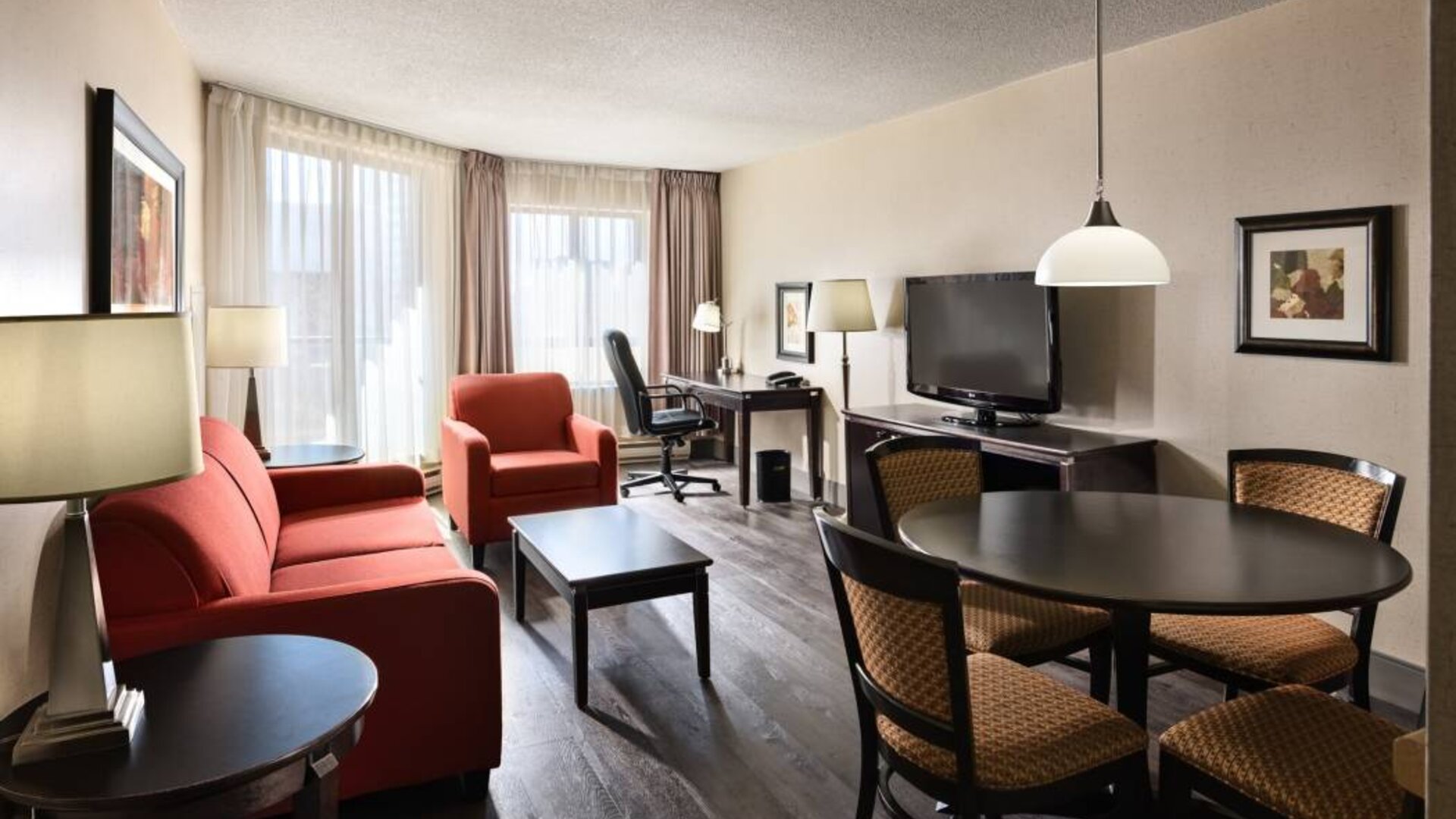 Guest room lounge in Les Suites Hotel Ottawa, with workspace desk and chair, plus sofa, chairs, and tables.