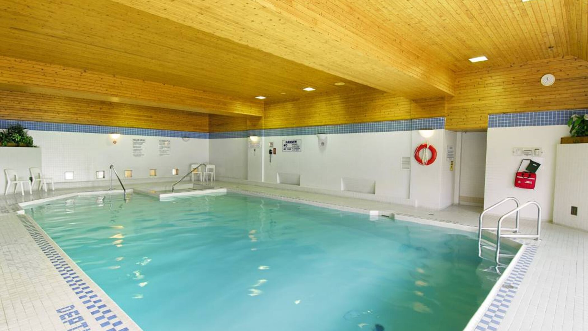 The hotel’s indoor pool is brightly lit and has chairs by the side.