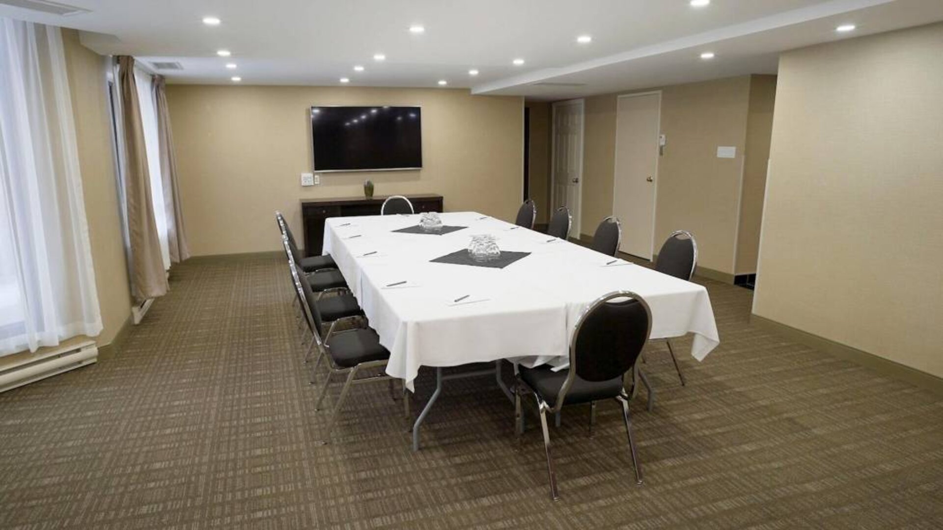 Meeting room in Les Suites Hotel Ottawa, with long table, ten chairs around it, and a large television.