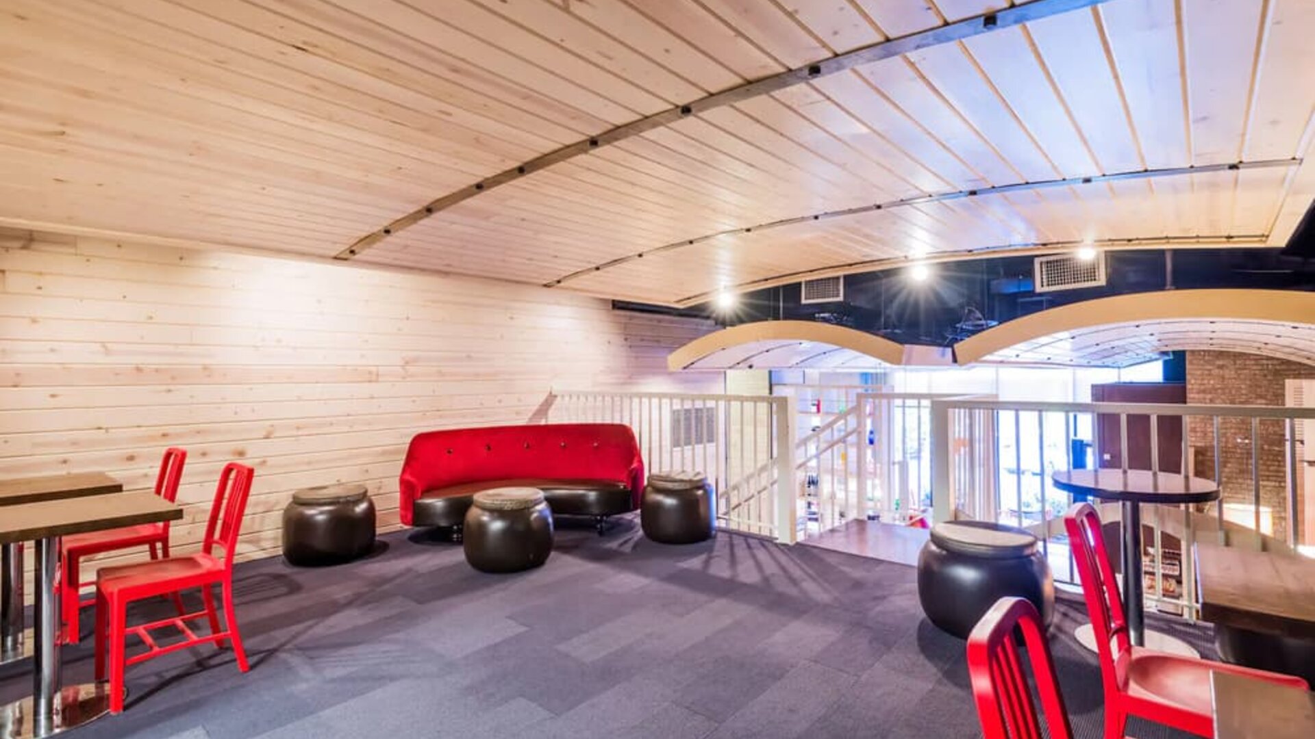 Second floor loft with arc planked ceiling, blue carpet, red chairs and small tables to work or socialize from.