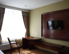 A Queens Hotel guest room with chair and table for working, and a nearby window.