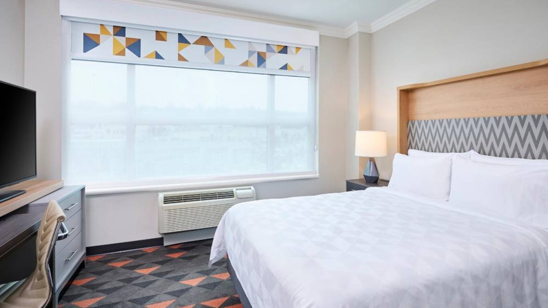 Double bed guest room in Holiday Inn & Suites Oakville At Bronte, with large window and bedside lamp.