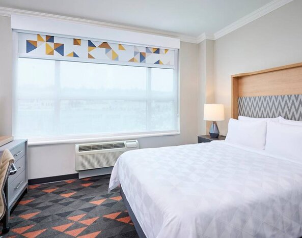 Double bed guest room in Holiday Inn & Suites Oakville At Bronte, with large window and bedside lamp.