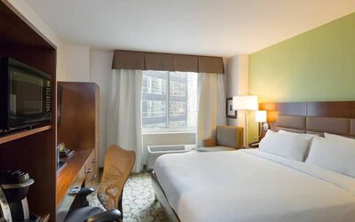 Hilton Garden Inn Midtown East guest room featuring large bed, big windows, and workspace chair and desk.