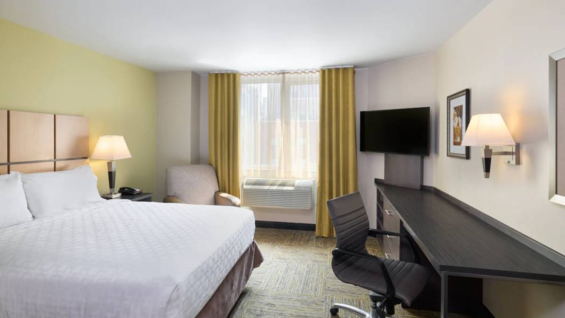 Double bed guest room in the Candlewood Suites Times Square, with workspace nearby and large window.