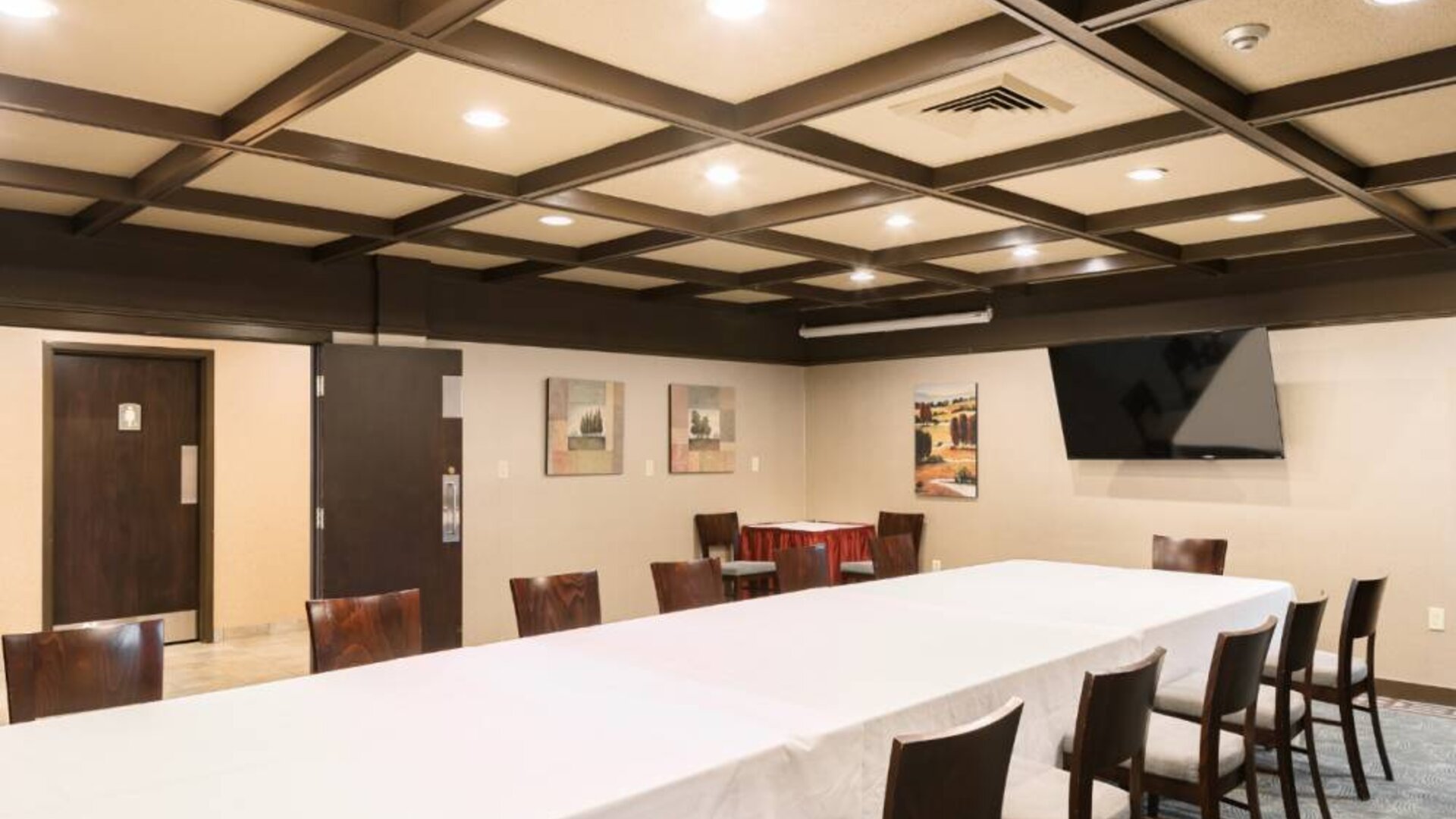 Hotel meeting room, featuring long table, surrounding chairs, and large TV.