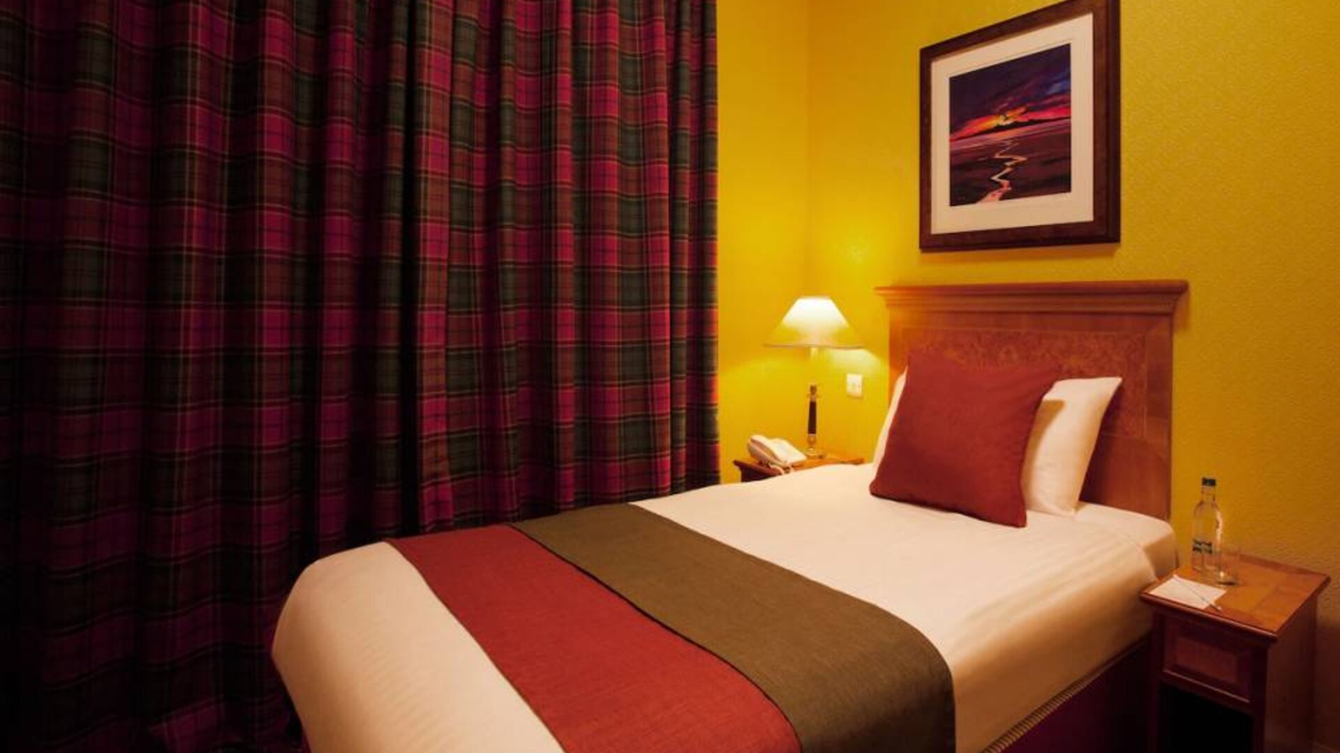 Single bed guest room in The Royal Highland Hotel, with bedside lamp and art on the wall.