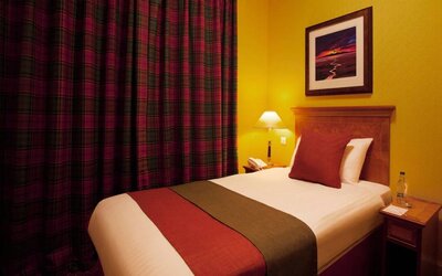 Single bed guest room in The Royal Highland Hotel, with bedside lamp and art on the wall.