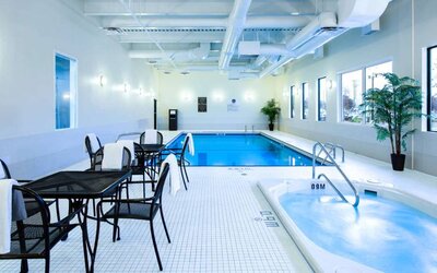 The hotel’s indoor swimming pool has tables, chairs, potted plants, and a hot tub nearby.