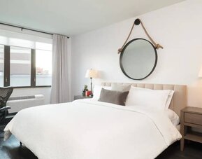 The Hilton Garden Inn Tribeca’s penthouse suite guest room, with large bed, window, and workspace.