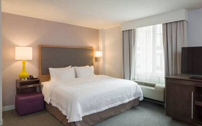 One of the Hampton Inn Times Square South’s king bed guest rooms, with window, TV, and bedside table.