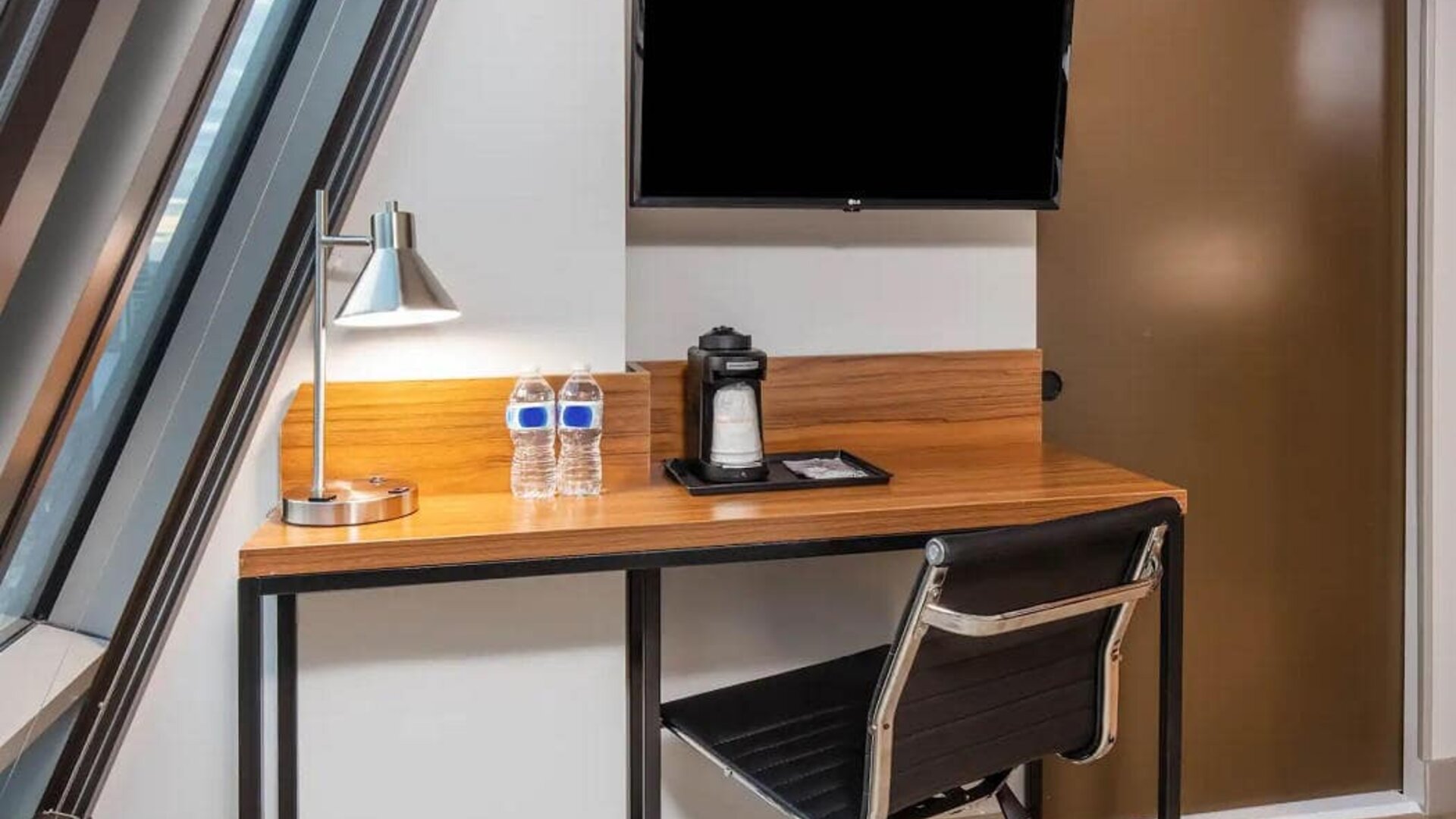 An in-room workspace at La Quinta Times Square South, with desk, chair, lamp, and TV.