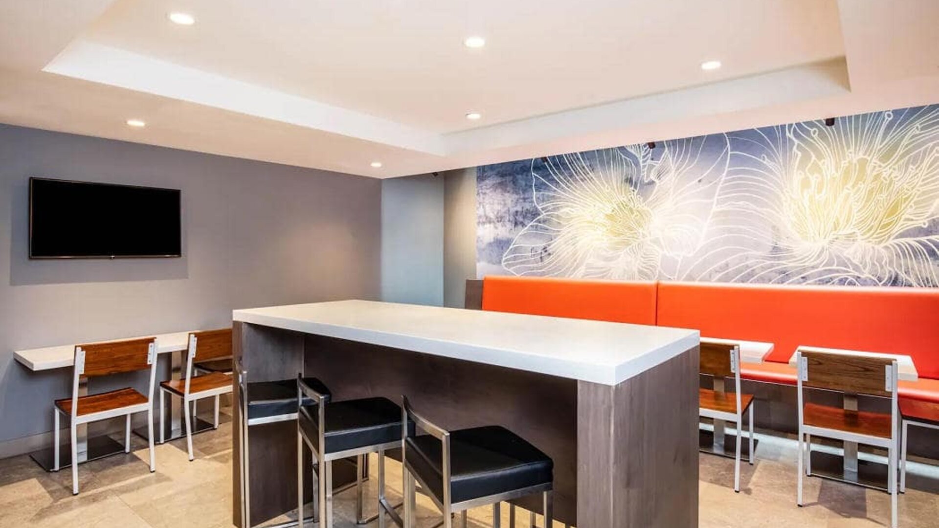 The hotel’s breakfast area, with hard floor, regular chairs and tables, and tall stools.